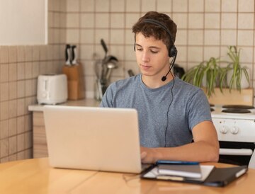 A man with headphones sits at a table, focused on his laptop, engaged in work or leisure activities.