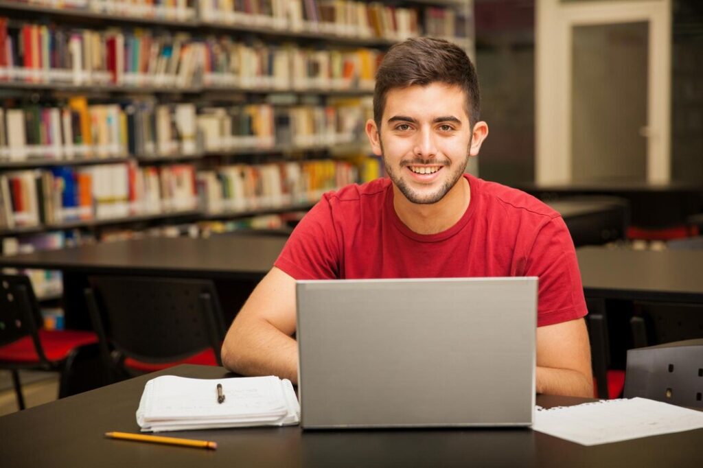 A young man smiles while working on his laptop, conveying a sense of enjoyment and engagement with his task.